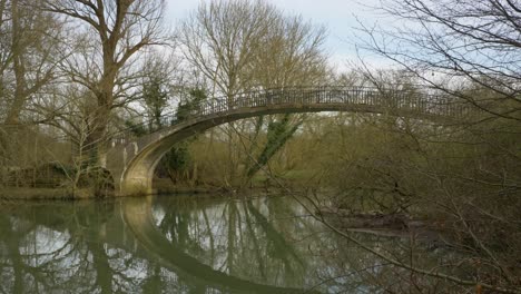 Tracking-Shot-Along-River-Bank-Looking-at-Footbridge-