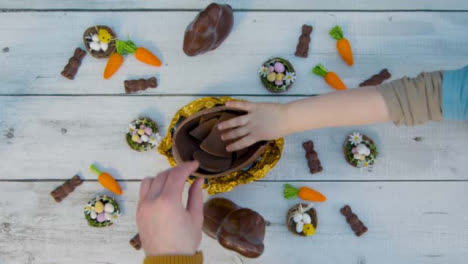 Overhead-Shot-of-Adult-and-Children's-Hands-Taking-Pieces-of-Chocolate-Egg-from-Table