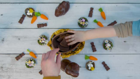 Fotografía-Cenital-De-Manos-De-Niños-Y-Adultos-Tomando-Trozos-De-Huevo-De-Chocolate-De-La-Mesa