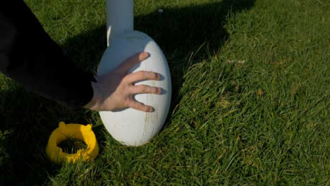 Close-Up-Shot-of-Rugby-Ball-and-Tee-Being-Placed-Next-to-Rugby-Post