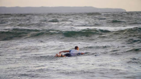 Handheld-Long-Shot-of-Surfer-Swimming-Out-to-Sea