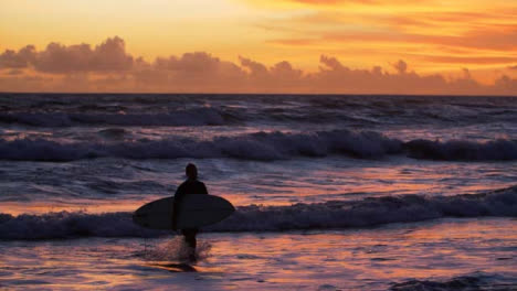 Handheld-Wide-Shot-Tracking-Surfer-Walking-Out-of-Water-at-Sunset