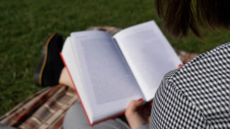Sliding-Over-the-Shoulder-Shot-of-Young-Woman-Reading-Book-In-Park