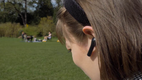 Close-Up-Shot-of-Young-Woman-Placing-Earphone-In-Her-Ear-In-Park