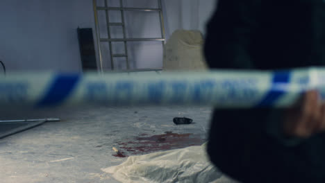 Sliding-Wide-Shot-of-Crime-Scene-In-Warehouse-with-Police-Tape-Being-Pulled-In-Foreground