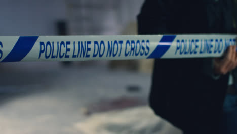 Sliding-Close-Up-Shot-of-Detective-Pulling-Police-Tape-In-Disused-Warehouse