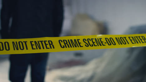 Close-Up-Shot-of-Detective-Walking-Underneath-Crime-Scene-Tape-In-Disused-Warehouse