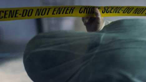 Close-Up-Shot-of-Forensic-Walking-Underneath-Crime-Scene-Tape-In-Disused-Warehouse