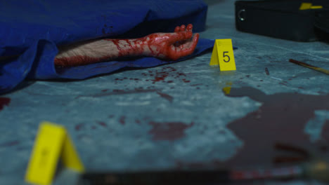 Sliding-Close-Up-Shot-of-Bloody-Hand-Underneath-Tarpaulin-at-Crime-Scene