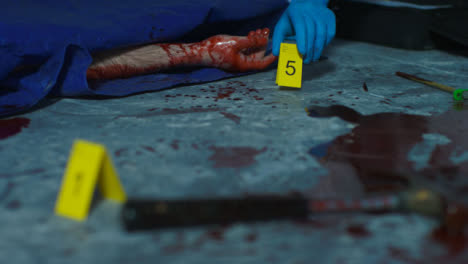 Sliding-Close-Up-Shot-of-Evidence-Tag-Being-Placed-Next-to-Bloody-Hand-at-Crime-Scene
