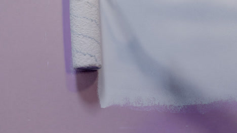 Close-Up-Shot-of-Paint-Roller-Applying-White-Paint-to-Pink-Wall-