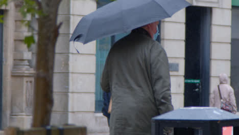 Panning-Shot-Following-Senior-Man-with-Umbrella-In-Rain