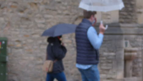 Defocused-Shot-of-Two-People-Walking-with-Umbrellas-In-Rain