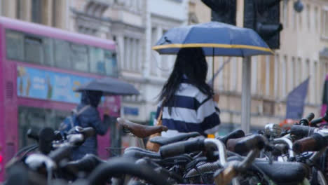 Low-Angle-Shot-Vorbei-An-Fahrradständer-Einer-Frau-Mit-Regenschirm