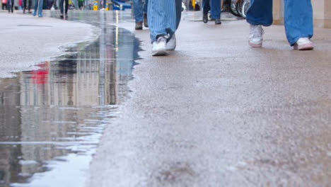 Podestaufnahme-Von-Regen,-Der-In-Eine-Pfütze-Fällt,-Während-Fußgänger-Vorbeigehen
