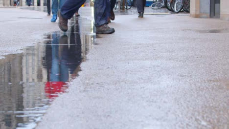 Toma-De-Pedestal-De-Lluvia-Cayendo-En-Un-Charco-Mientras-La-Gente-Camina-Junto-A-él