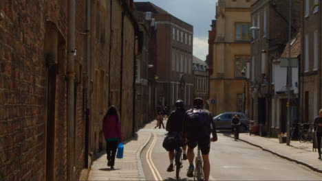 Tracking-Shot-of-Cyclists-Riding-Down-Quiet-Old-English-Backstreet