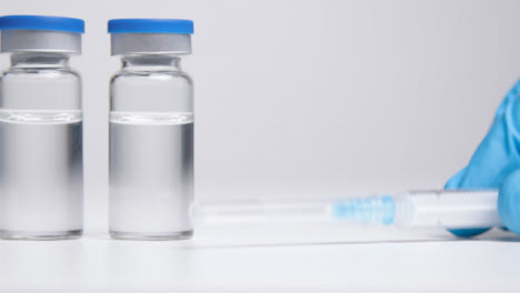 Sliding-Shot-Along-Line-of-Vials-of-Translucent-Liquid-and-a-Syringe-Before-Hand-Takes-It-Away