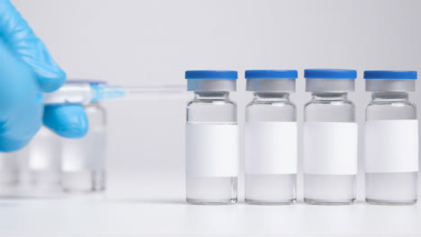 Close-Up-Shot-of-Line-of-Vials-of-with-Clean-White-Labels-and-a-Syringe-Before-Hand-Takes-It-Away