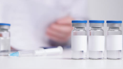 Close-Up-Shot-of-Vials-with-Clean-White-Labels-as-Medical-Professional-Works-In-the-Background