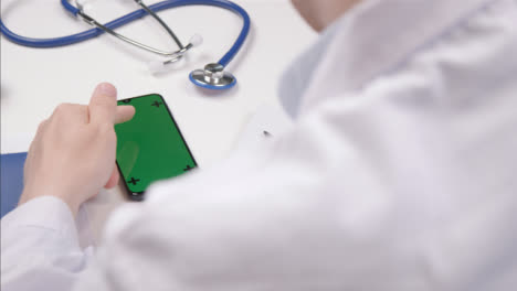 Over-the-Shoulder-Shot-of-a-Medical-Professional-Using-Smartphone-Touchscreen-with-Green-Screen