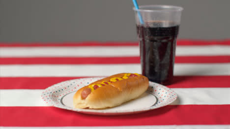 Sliding-Shot-of-Hot-Dog-and-Soda-On-Striped-Table-Cloth