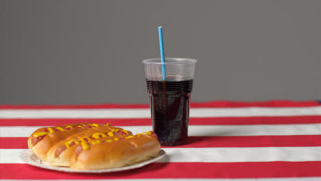 Sliding-Shot-of-Hot-Dogs-and-Soda-On-Striped-Table-Cloth