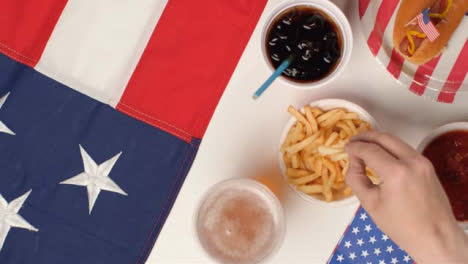 Top-Down-Shot-of-Hands-Taking-Fries-and-Beer-from-July-4th-Party-Food-Spread