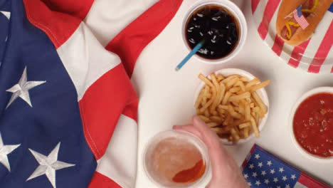 Top-Down-Shot-of-Hands-Taking-Fries-and-a-Beer-from-a-July-4th-Party-Food-Spread