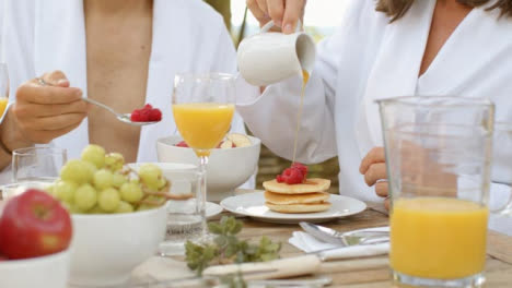 Medium-Shot-of-Middle-Aged-Woman-Pouring-Syrup-On-Pancakes-During-Breakfast