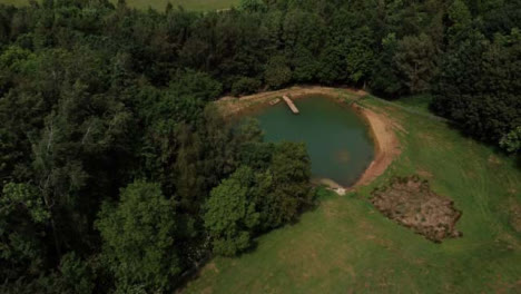 Drone-Shot-Flying-Away-from-Scenic-Lake-On-Edge-of-Woodland
