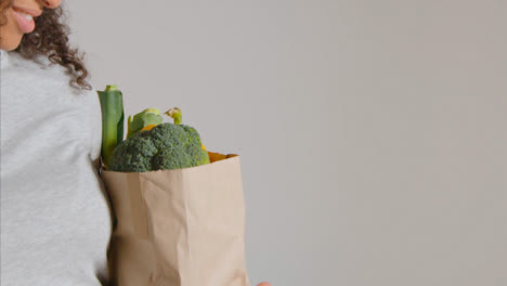 Side-Profile-Shot-of-Young-Adult-Woman-Holding-Brown-Paper-Bag-of-Vegetables