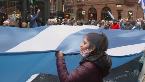 Handheld-Shot-of-Climate-Change-Protesters-Marching-Through-Glasgow-with-a-Giant-Scottish-Flag
