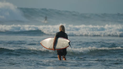 Lange-Aufnahme-Eines-Surfers,-Der-Auf-Bali-Ins-Meer-Geht