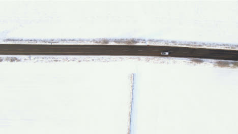 Drone-Shot-Looking-Down-On-a-Road-Between-Snowy-Fields-