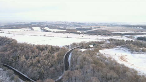 Drone-Shot-Flying-Over-Road-and-Snowy-Woodland