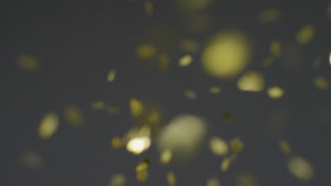 Stationary-Shot-of-Gold-Confetti-Falling-Against-a-Grey-Background