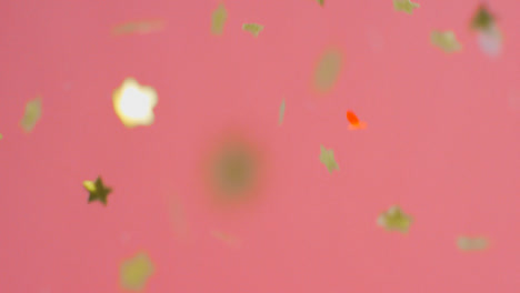 Stationary-Shot-of-Coloured-and-Gold-Confetti-Falling-Against-Pink-Background