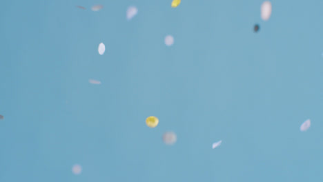 Stationary-Shot-of-Grey-and-Gold-Confetti-Falling-Against-a-Blue-Background