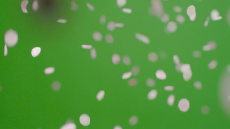 Stationary-Shot-of-Pink-Confetti-Falling-Against-Green-Background