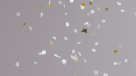Stationary-Shot-of-White-and-Gold-Confetti-Falling-Against-Grey-Background