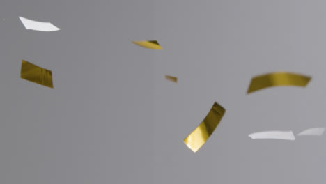 Stationary-Shot-of-Gold-and-White-Confetti-Falling-Against-a-Grey-Background