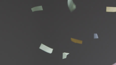 Stationary-Shot-of-Coloured-and-Gold-Strip-Confetti-Falling-Against-a-Grey-Background