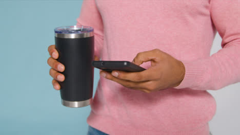 Close-Up-Shot-of-Young-Adult-Mans-Hands-Holding-Flask-and-Using-Smartphone