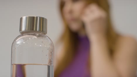 Close-Up-Shot-of-Bottle-with-Woman-Working-in-Background