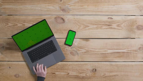 Top-Down-Shot-of-Person-Working-On-Green-Screen-MacBook-with-Green-Screen-Smartphone
