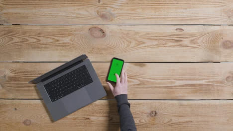 Top-Down-Shot-of-Person-Working-On-MacBook-with-Green-Screen-Smartphone