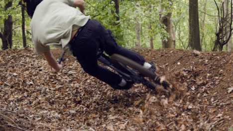 Low-Angle-Shot-Of-Man-On-Mountain-Bike-Cycling-Along-Dirt-Trail-Through-Leaves-In-Woodland