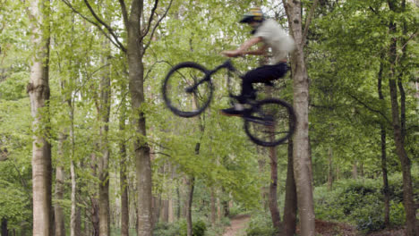 Toma-En-Cámara-Lenta-De-Un-Hombre-En-Bicicleta-De-Montaña-Haciendo-Un-Salto-En-El-Aire-En-Un-Sendero-De-Tierra-A-Través-Del-Bosque-3