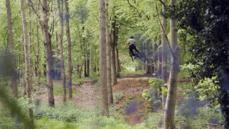 Slow-Motion-Shot-Of-Man-On-Mountain-Bike-Making-Mid-Air-Jump-On-Dirt-Trail-Through-Bluebell-Woods